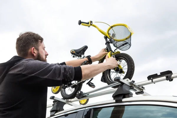 Cykeltransport-en man fäster och installerar en barnens cykel på taket av en bil i ett speciellt fäste för cykeltransport. Beslutet att transportera stora laster och resa med bil. — Stockfoto