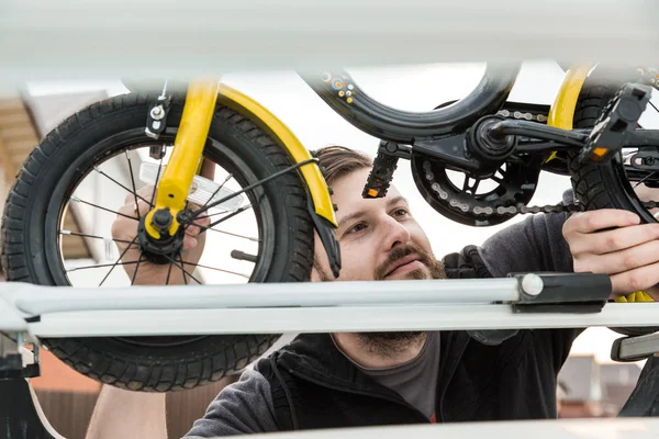 Cykeltransport-en man fäster och installerar en barnens cykel på taket av en bil i ett speciellt fäste för cykeltransport. Beslutet att transportera stora laster och resa med bil. — Stockfoto