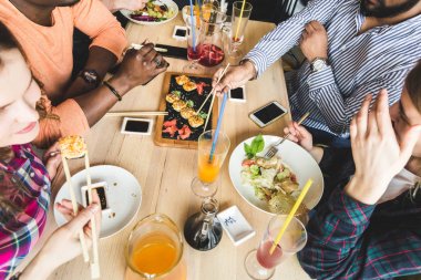 Üst te. Bir kafede çok kültürlü şirket gençlerin bir şirket suşi rulo yeme, eğlenmek içki içme