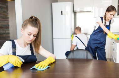 İş sırasında profesyonel ekipmanlarla temizlik hizmeti. Profesyonel mutfak temizliği, kanepe kuru temizleme, pencere ve yer silme. Erkek ve kadın üniformalı, tulumlu ve lastik eldivenli.
