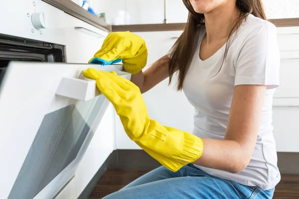 Eine junge Frau von einer professionellen Reinigungsfirma räumt zu Hause auf. Ein Mann wäscht die Küche in gelben Handschuhen mit Putzmitteln. — Stockfoto