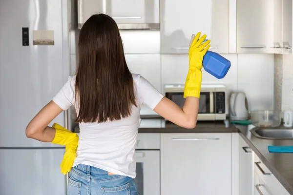 Een jonge vrouw van een professioneel schoonmaakbedrijf ruimt thuis op. Een man wast de keuken in gele handschoenen met schoonmaakspullen. — Stockfoto