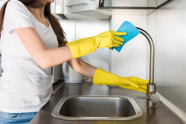 Una joven con guantes amarillos lava la grúa con una esponja en el fregadero. Servicio de limpieza profesional de casas —  Fotos de Stock