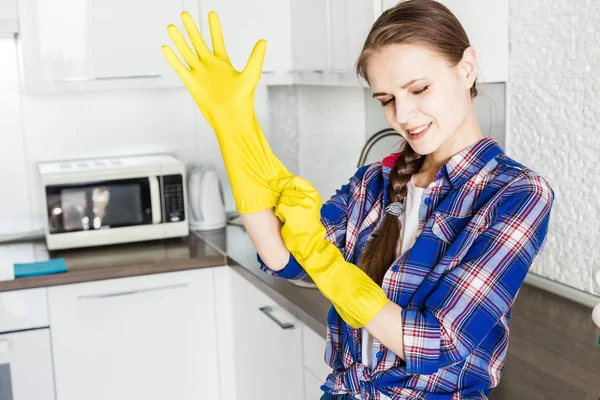 Μια νεαρή γυναίκα καθαρίζει στο σπίτι, πλένει την κουζίνα. Κουβάς με κουρέλια και κίτρινα γάντια στο τραπέζι — Φωτογραφία Αρχείου