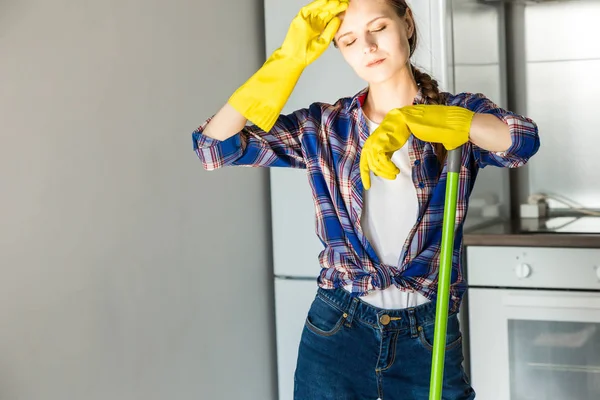 Una joven hace la limpieza en casa, lava la cocina. Cubo con trapos y guantes amarillos en la mesa —  Fotos de Stock