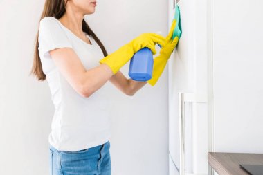 Profesyonel temizlik şirketinden genç bir kadın evi temizliyor. Bir adam mutfağı yıkıyor ve buzdolabını sarı eldivenlerle temizliyor..