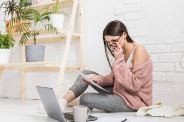 Genç ve mutlu bir kadın parlak bir apartman dairesinde ya da ofis içinde yerde oturuyor ve bir dizüstü bilgisayarda çalışıyor, iş yerinde serbest çalışan bir kız, uzaktan öğrenme öğrencileri, evrak işleri ve çevrimiçi öğrenim kavramı