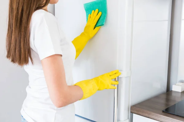 Uma jovem de uma empresa de limpeza profissional limpa em casa. Um homem lava a cozinha lava o frigorífico com luvas amarelas com material de limpeza. . — Fotografia de Stock