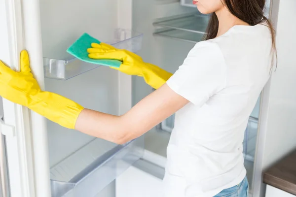 Uma jovem de uma empresa de limpeza profissional limpa em casa. Um homem lava a cozinha lava o frigorífico com luvas amarelas com material de limpeza. . — Fotografia de Stock