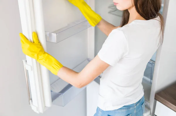 Profesyonel temizlik şirketinden genç bir kadın evi temizliyor. Bir adam mutfağı yıkıyor ve buzdolabını sarı eldivenlerle temizliyor.. — Stok fotoğraf