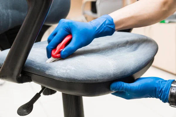 Jongeman in werkkleding en rubberen handschoenen reinigt de bureaustoel met professionele apparatuur. — Stockfoto