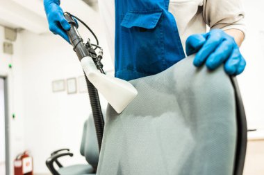 İş elbiseli ve lastik eldivenli genç adam ofis sandalyesini profesyonel ekipmanlarla temizliyor..