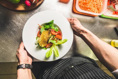 Oteldeki mutfak restoranında yemek pişiren profesyonel bir aşçı. Yemek hazırlıyor. Önlüklü bir aşçı sebze ve pizzadan salata yapar..