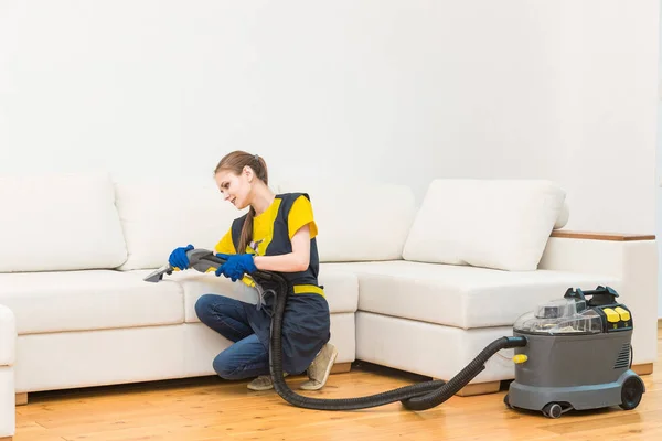 Professionele schoonmaak. Twee vrouwen in uniform, in schorten. Twee vrouwen in een werkend uniform, in schorten, verdelen de schoonmaak van een privéhuis, een huisje. Wassen, stofzuigen van de bank — Stockfoto