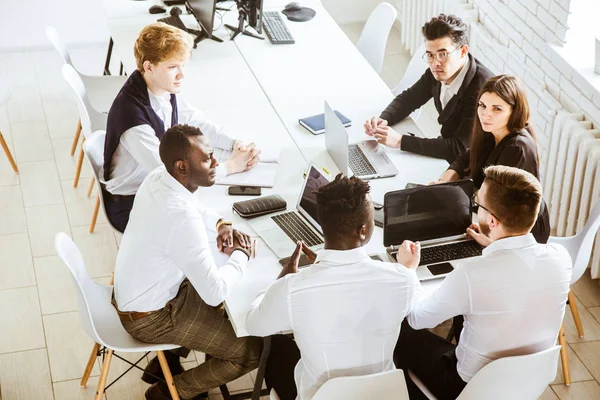 Un equipo de jóvenes empresarios sentados a la mesa, con vista superior, trabajando y comunicándose juntos en una oficina. Corporativossteam y gerente en una reunión . — Foto de Stock