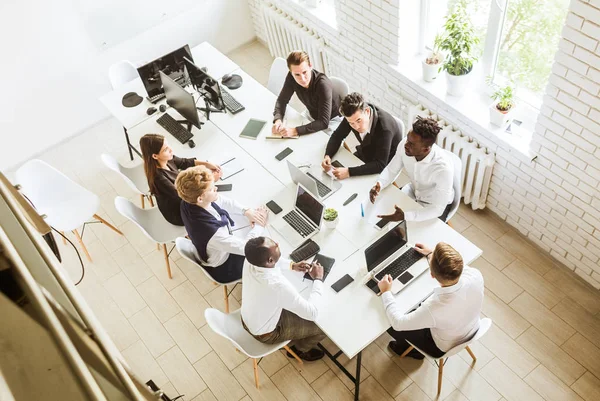 Un equipo de jóvenes empresarios sentados a la mesa, con vista superior, trabajando y comunicándose juntos en una oficina. Corporativossteam y gerente en una reunión . — Foto de Stock