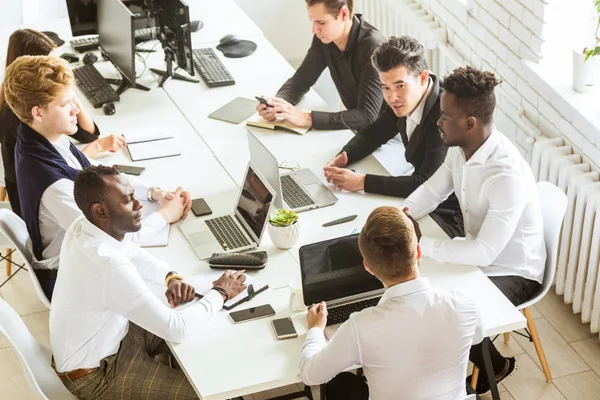 Un equipo de jóvenes empresarios sentados a la mesa, con vista superior, trabajando y comunicándose juntos en una oficina. Corporativossteam y gerente en una reunión . — Foto de Stock