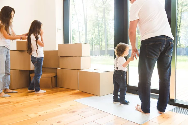 Feliz familia joven, padres hija e hijo, desempacando cajas y mudarse a un nuevo hogar. niños divertidos corren con cajas — Foto de Stock