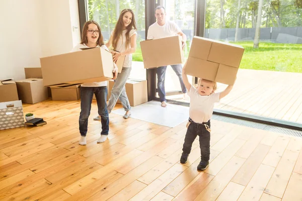 Giovane famiglia felice, i genitori figlia e figlio, disfare le scatole e trasferirsi in una nuova casa. bambini divertenti corrono dentro con scatole — Foto Stock