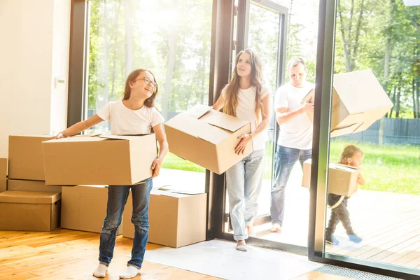 Lycklig ung familj, föräldrar dotter och son, packa upp lådor och flytta in i ett nytt hem. roliga barn springer in med lådor — Stockfoto