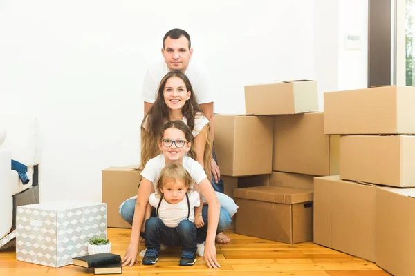 Lycklig ung familj, föräldrar dotter och son, packa upp lådor och flytta in i ett nytt hem. roliga barn springer in med lådor — Stockfoto