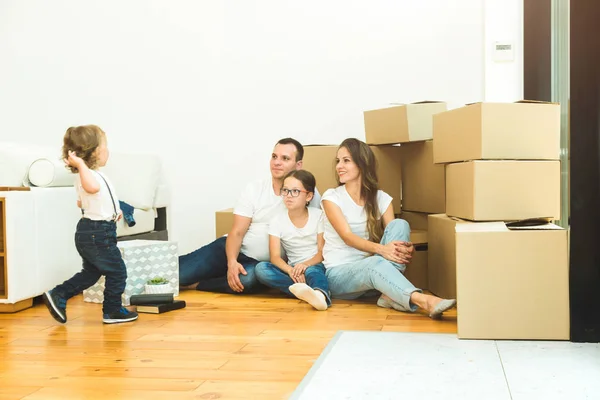 Feliz familia joven, padres hija e hijo, desempacando cajas y mudarse a un nuevo hogar. niños divertidos corren con cajas — Foto de Stock