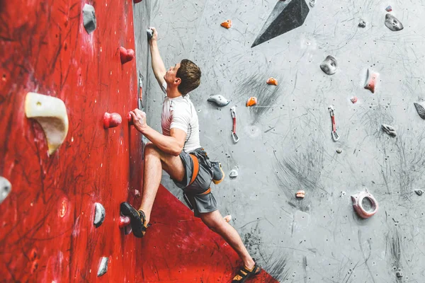 Deportista escalador ascendiendo en roca escarpada, escalando en la pared artificial en el interior. Concepto de deportes extremos y bouldering — Foto de Stock