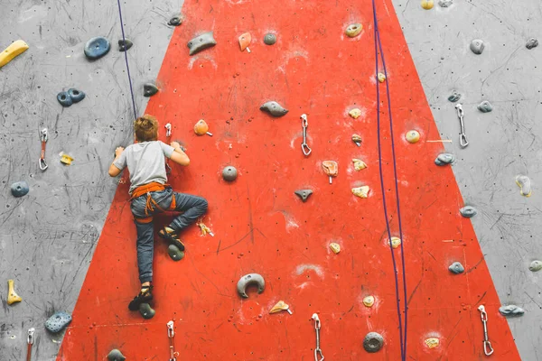 Kid alpinista se movendo em rocha íngreme, escalando na parede artificial dentro de casa. Conceito de esportes radicais e bouldering — Fotografia de Stock