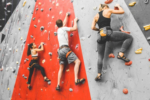 Atletas escalador ascendiendo en roca escarpada, escalando en la pared artificial en el interior. Concepto de deportes extremos y bouldering — Foto de Stock