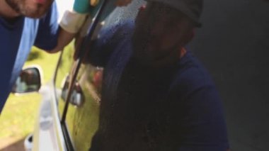Profesyonel araba temizliği. Eldivenli bir adam arabanın renkli camını temizler ve siler ve ona yansıtır. Veritabanı