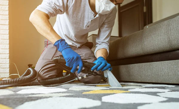 Male worker removing dirt from carpet with professional vacuum cleaner indoors