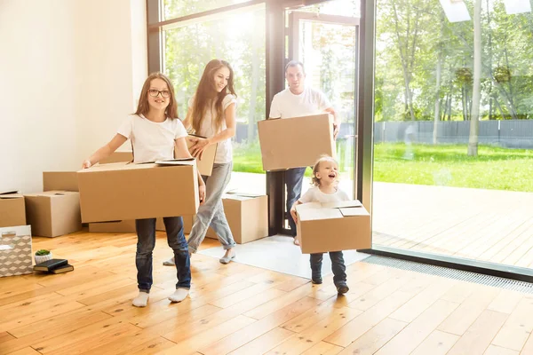 Lycklig ung familj, föräldrar dotter och son, packa upp lådor och flytta in i ett nytt hem. roliga barn springer in med lådor — Stockfoto