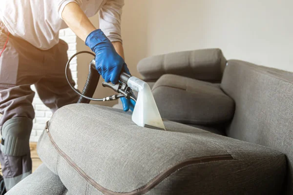 Reinigungsservice. Mann Hausmeister in Handschuhen und Uniform staubsaugen Sofa mit professioneller Ausrüstung — Stockfoto