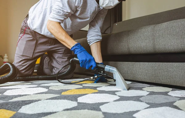 Pekerja laki-laki mengeluarkan kotoran dari karpet dengan vacuum cleaner profesional di dalam ruangan — Stok Foto