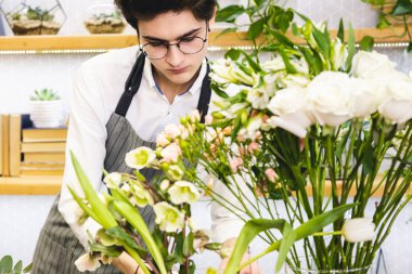 Çiçekçide çalışan gözlüklü ve önlüklü çekici bir erkek çiçekçi..