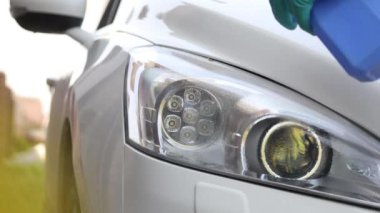 Araba temizliği. Eldivenli bir adam arabanın farlarını temizliyor ve parlamak için siliyor..