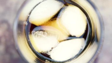 Bulanık bir yaz yeşilliği arka planında buzlu ve köpüren sıvıyla ferahlatıcı soğuk bir içecek içeren bir bardağın yakın çekimi.