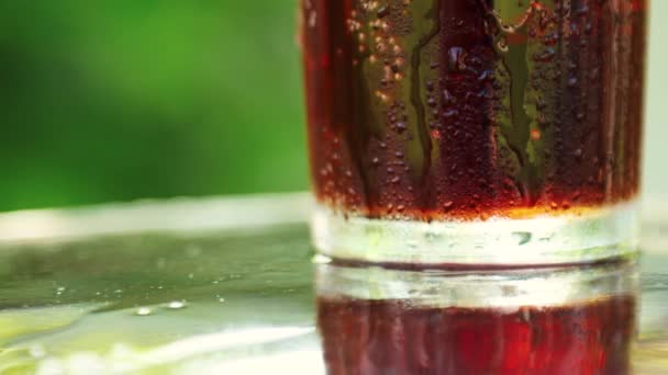 Close-up van een glas met een verfrissend koud drankje met stukjes ijs en borrelende vloeistof op een wazig zomerbladerdek — Stockvideo