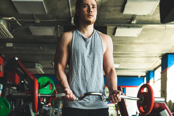 Retrato de um jovem atleta muscular executa exercícios com um sino na academia. Treinamento de força de resistência — Fotografia de Stock