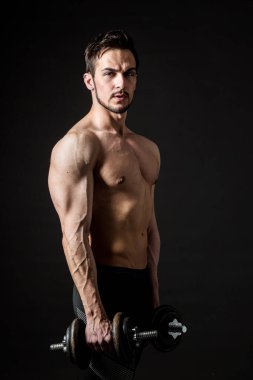 Koyu arkaplanda dambıllarla poz veren çekici kas sporcusu..