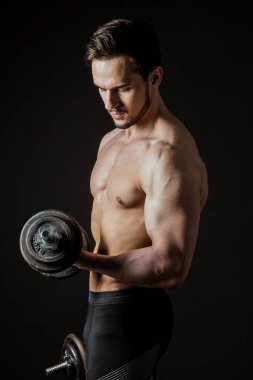 Koyu arkaplanda dambılları olan çekici kaslı bir sporcunun portresi.