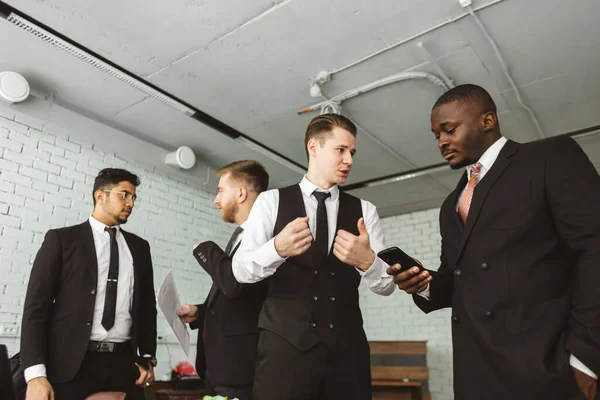 Diálogo de dos hombres con smartphones jóvenes empresarios en trajes trabajando y comunicándose juntos en una oficina. Corporativossteam y gerente en una reunión. — Foto de Stock
