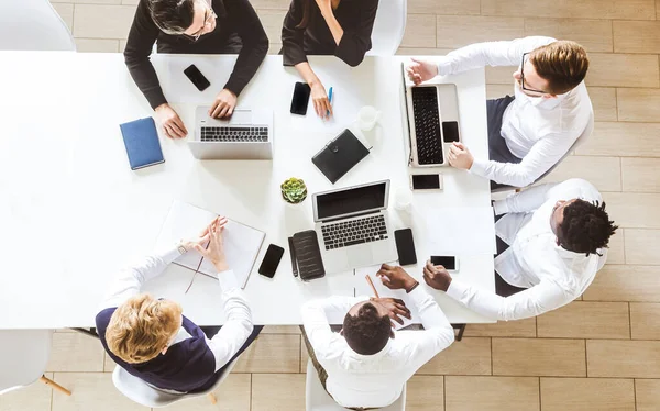 Un equipo de jóvenes empresarios sentados a la mesa, con vista superior, trabajando y comunicándose juntos en una oficina. Corporativossteam y gerente en una reunión . — Foto de Stock