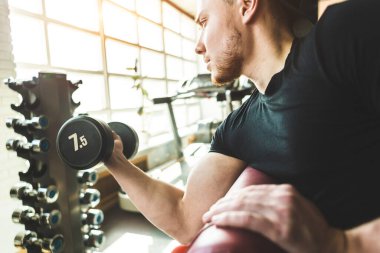Kaslı bir adamın portresi spor salonunda egzersiz yapıyor. Dambıllarla antreman