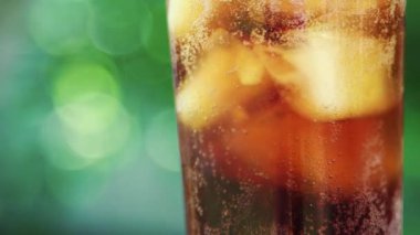 Bulanık bir yaz yeşilliği arka planında buzlu ve köpüren sıvıyla ferahlatıcı soğuk bir içecek içeren bir bardağın yakın çekimi.