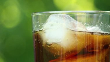 Bulanık bir yaz yeşilliği arka planında buzlu ve köpüren sıvıyla ferahlatıcı soğuk bir içecek içeren bir bardağın yakın çekimi.