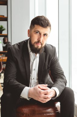 Ofiste takım elbiseli başarılı bir iş adamının portresi. Pencerenin yanındaki sandalyede otururken.