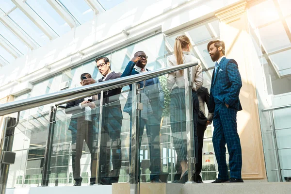 Jóvenes empresarios están de pie y hablando en el fondo de las oficinas de vidrio. Corporativossteam y gerente en una reunión. — Foto de Stock