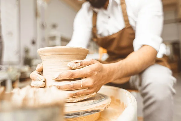 Um jovem oleiro masculino trabalha em sua oficina em uma roda de oleiros e faz produtos de argila. Close-up de mãos — Fotografia de Stock