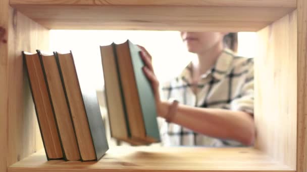 Egy fiatal nő könyvespolcokat porol. Takarítás és napi házimunka — Stock videók